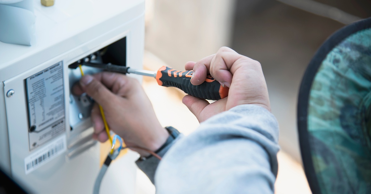 A person uses a screwdriver to connect wires inside an electrical unit, performing maintenance or installation work.