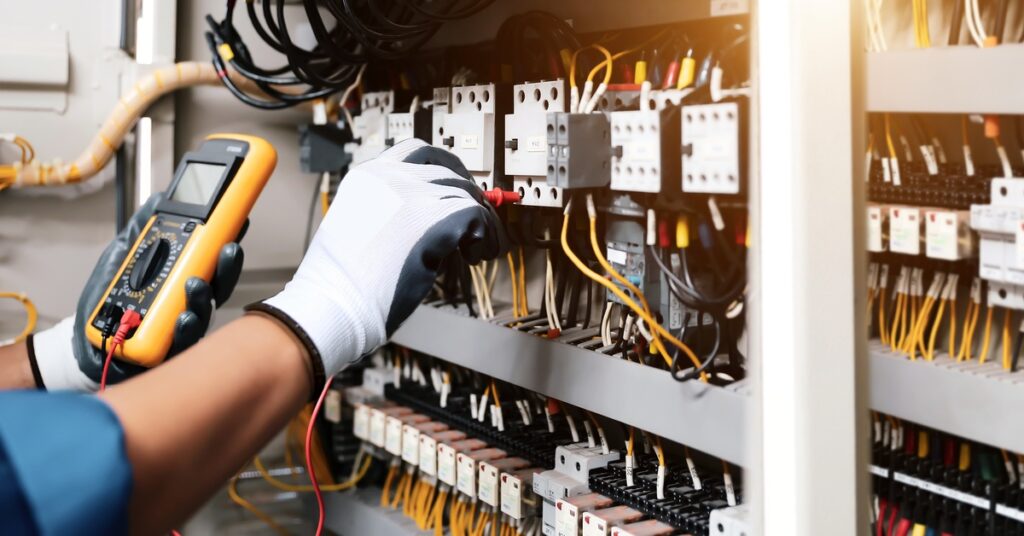 A technician uses a multimeter to test electrical connections inside a control panel with organized wiring.