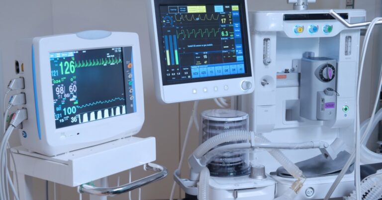 Hospital patient monitors and ventilator equipment display vital signs and respiratory data in a medical care setting.