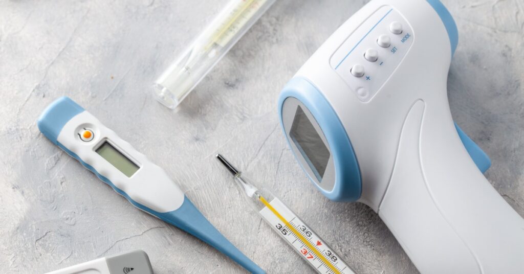 A collection of digital and infrared thermometers arranged on a surface, representing temperature measurement tools.
