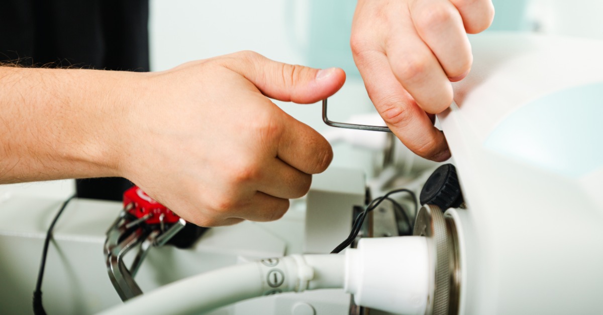 A technician uses a hand tool to adjust a component inside an opened piece of equipment during maintenance.